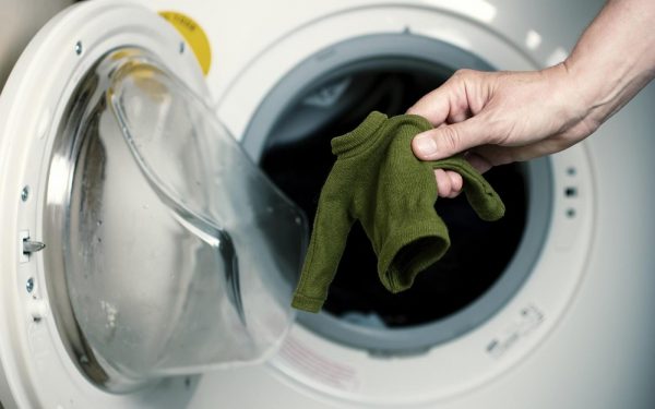 Рука держит маленький свитер на фоне стиральной машинки